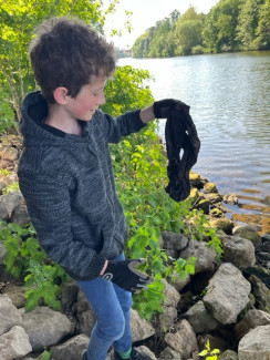 Junge steht am Ufer und hält einen Stofffetzen in die Luft
